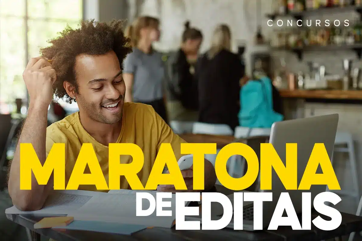 Maratona de Editais para Concursos Jovem sorrindo enquanto estuda para concursos, com livros e laptop em uma mesa.