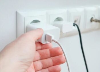 Pessoa conectando carregador à tomada, ilustrando a importância de desligar aparelhos eletrônicos durante tempestades e surtos elétricos.