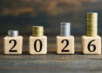 Pilhas de moedas crescentes sobre blocos de madeira com o número 2026, simbolizando o início da transição da Reforma Tributária e o aumento da arrecadação/economia.