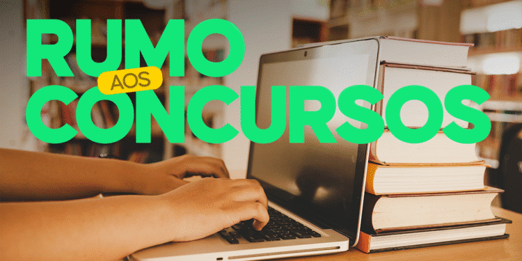 Pessoa estudando para concursos com computador e livros empilhados em biblioteca