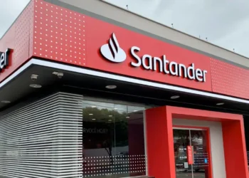 Imagem de uma agência do Santander, destacando a fachada moderna, com o logo e o convite para novas oportunidades de trabalho. Vagas abertas até 15 de outubro.