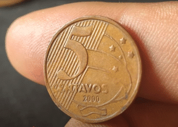 Close-up de uma mão segurando uma moeda de 5 centavos do ano 2000, destacando a raridade do item para colecionadores.
