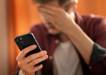 Pessoa com expressão de preocupação segurando um celular, possivelmente alertada por mensagem sobre um vírus de celular.