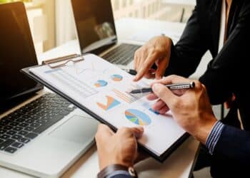 Mãos de dois profissionais analisando gráficos e relatórios em uma prancheta durante uma reunião de estratégia de negócios. O foco está nos dados de crescimento, alinhado à discussão sobre a expansão de 170 milhões de vagas em áreas como IA e sustentabilidade até o final da década.