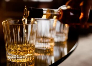 Homem servindo bebida alcoólica em copos, com foco na ação de despejar o líquido dourado.