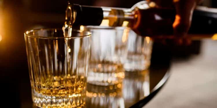 Homem servindo bebida alcoólica em copos, com foco na ação de despejar o líquido dourado.