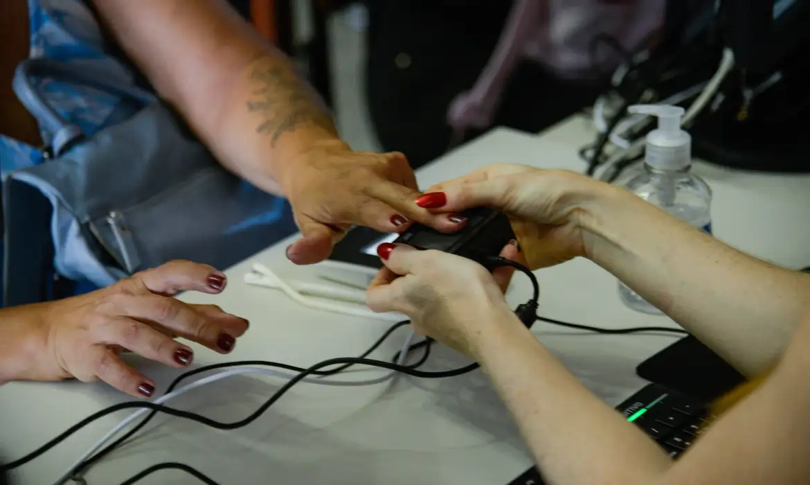 Mãos femininas segurando aparelho de medição de glicose em dedo de pessoa com esmalte vermelho