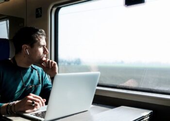 Profissional trabalhando em um laptop dentro de um trem, refletindo sobre o trabalho remoto enquanto viaja.