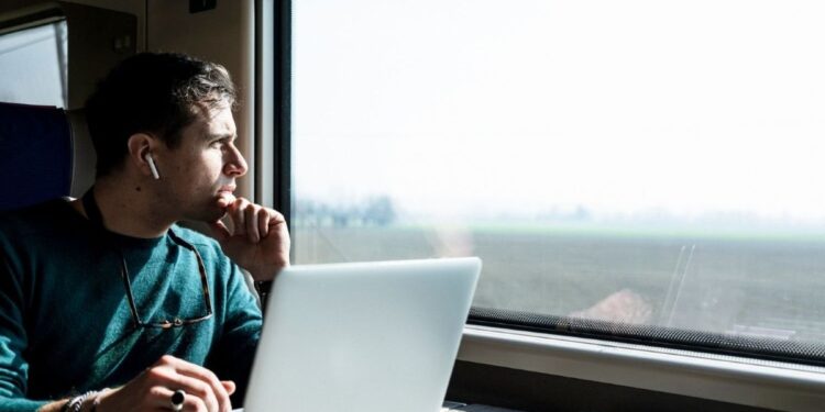 Profissional trabalhando em um laptop dentro de um trem, refletindo sobre o trabalho remoto enquanto viaja.