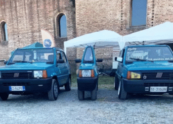 Dois Fiat Panda azuis e um microcarro azul entre eles em área externa com tende branca e parede de tijolos
