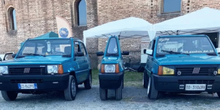 Dois Fiat Panda azuis e um microcarro azul entre eles em área externa com tende branca e parede de tijolos