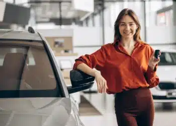 Mulher sorrindo com chave de carro usada em concessionária, destacando a importância de cuidados ao comprar carro usado de 2022.