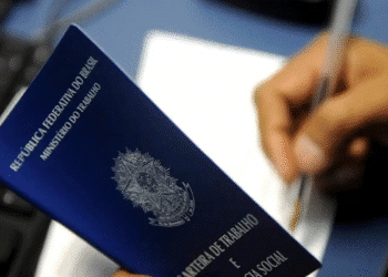 Carteira de Trabalho da República Federativa do Brasil sendo segurada enquanto uma pessoa escreve ou assina