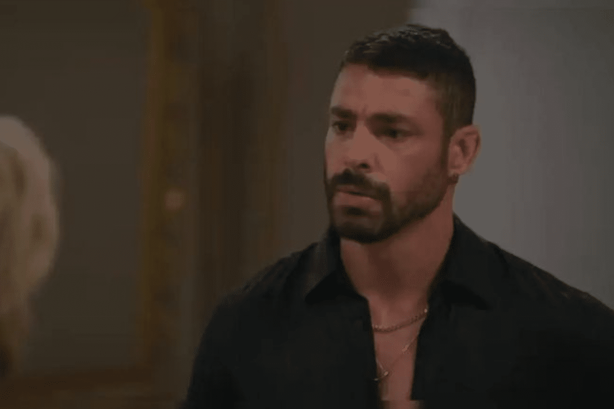 Homem com barba curta e cabelo preto, vestindo camisa preta, com expressão séria em ambiente interno.