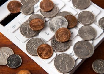 Moedas de centavos e quarters americanos espalhadas sobre um teclado de calculadora, simbolizando a avaliação e contagem de dinheiro. A imagem remete à análise do valor de moedas raras com erros de cunhagem.
