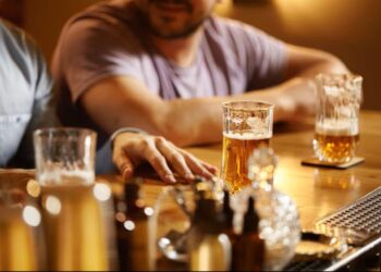 Homens em um bar com copos de cerveja, ilustrando o consumo de bebidas alcoólicas que podem estar contaminadas com metanol.