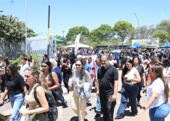 Grupo diversificado de pessoas caminhando em evento ao ar livre com céu azul e árvores ao fundo