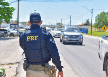 Agente da Polícia Rodoviária Federal vistoriando veículos em movimentada estrada durante o dia