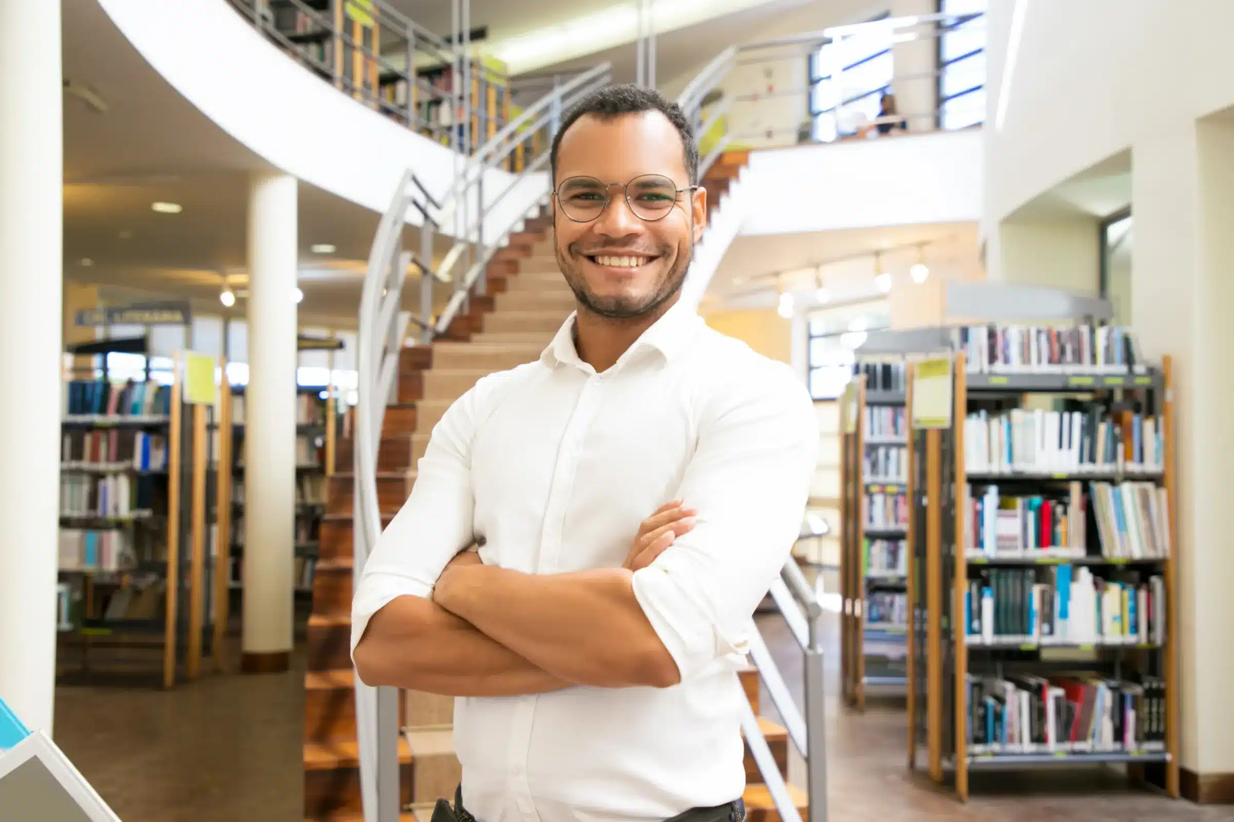 Inscrições abertas para o concurso público de professores Homem sorridente em biblioteca representando oportunidade de concurso para professores.