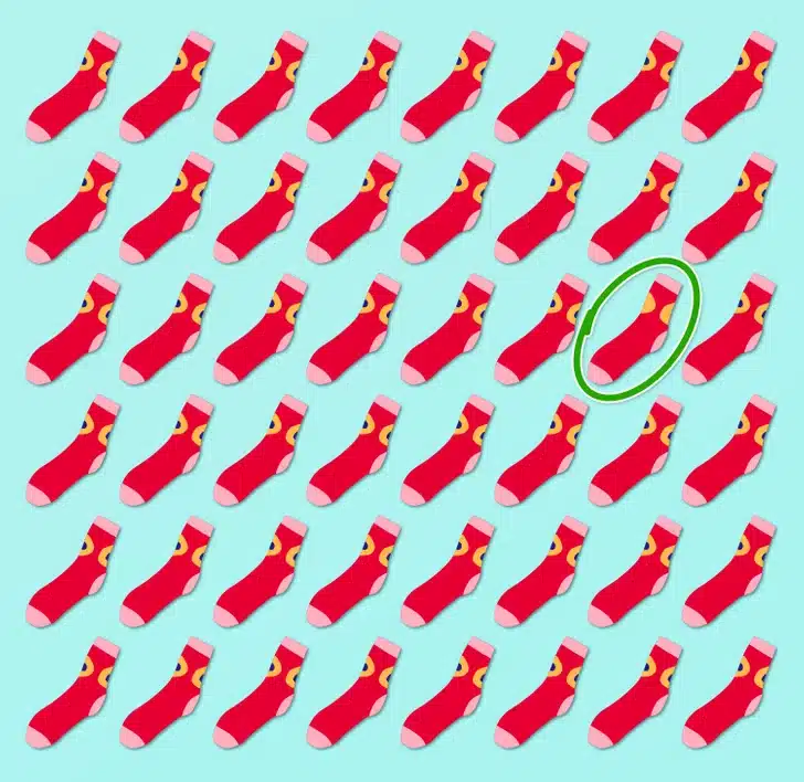 Ache a meia distinta entre várias meias vermelhas com detalhes amarelos em um padrão repetido. Desafio visual com várias meias vermelhas com detalhes amarelos e ponta rosa, organizadas em padrão sobre fundo azul claro