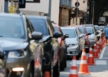 Vários carros estacionados em fila ao longo de uma calçada com cones laranja indicando delimitação