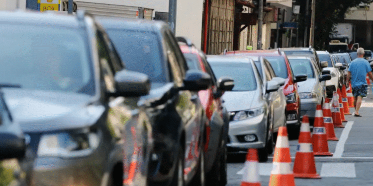 Vários carros estacionados em fila ao longo de uma calçada com cones laranja indicando delimitação