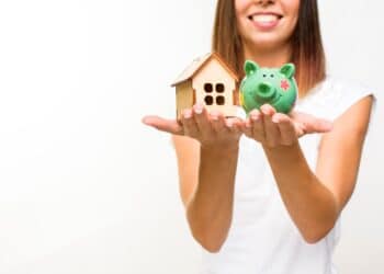Mulher segurando casa e porquinho de porcelana simbolizando empréstimo para reforma de casa.