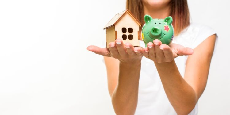 Mulher segurando casa e porquinho de porcelana simbolizando empréstimo para reforma de casa.