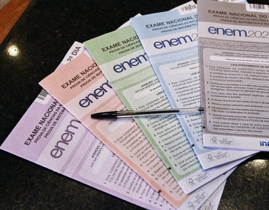 Cadernos de provas do Exame Nacional do Ensino Médio (ENEM) 2024, com caneta sobre a mesa.