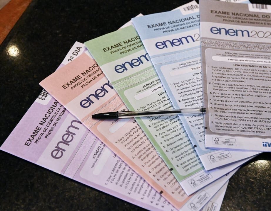 Cadernos de prova do Enem organizados por cor, com uma caneta sobre eles.