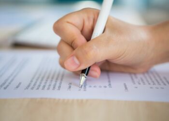 Pessoa assinando documento formal com caneta preta.