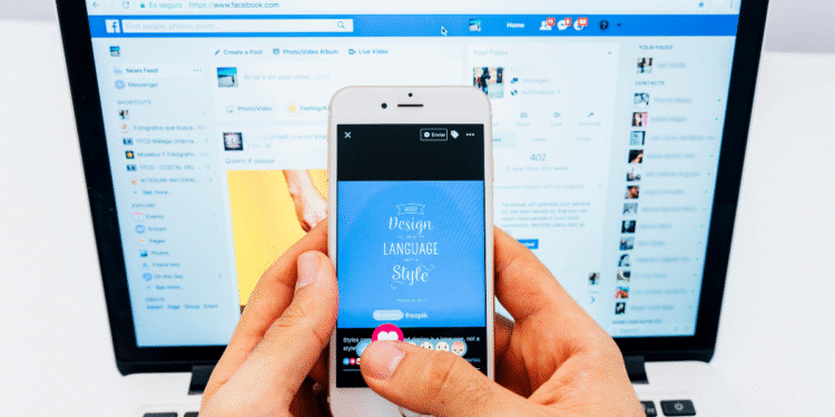 Pessoa segurando smartphone mostrando postagem no Facebook com laptop ao fundo exibindo a rede social.