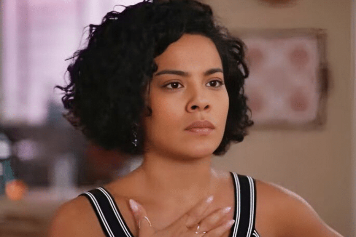  Mulher jovem de cabelos cacheados curtos, com expressão séria e pele morena clara, vestindo regata listrada preta e branca