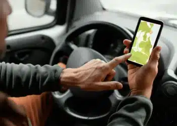 Imagem ilustrativa de uma pessoa utilizando aplicativo de mapas no celular enquanto dirige, com foco em zonas de risco.