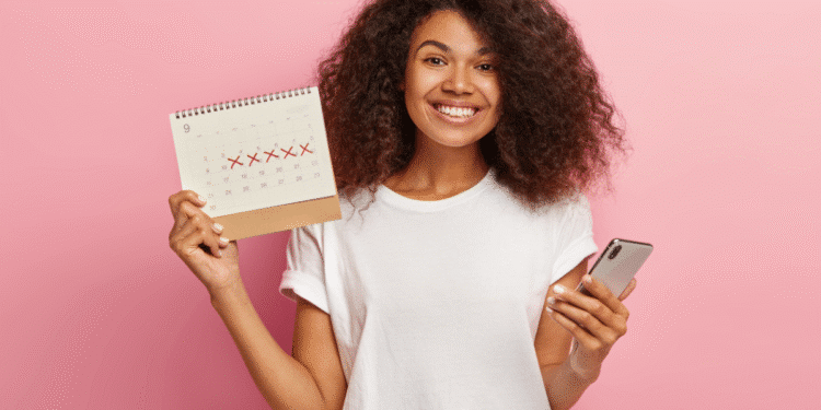 Jovem sorridente segurando calendário com dias riscados e celular na mão, fundo rosa