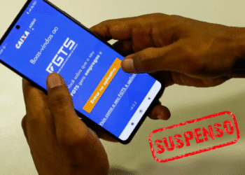 Pessoa segura celular com o aplicativo do FGTS aberto e a palavra “suspenso” em destaque.