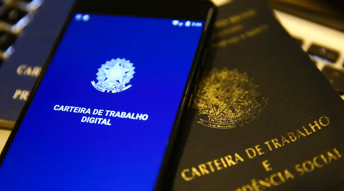 Mudança no saque-aniversário do FGTS é suspensa Celular com o aplicativo da Carteira de Trabalho Digital sobre uma carteira de trabalho física.