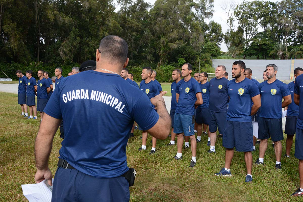 Guarda Municipal em formação durante treinamento ao ar livre, vestindo uniformes azuis em campo de grama