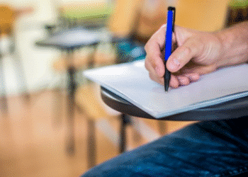 Pessoa escrevendo em folha de prova em uma sala de aula.