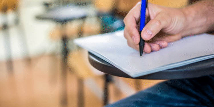 Pessoa escrevendo em folha de prova em uma sala de aula.