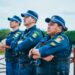 Três guardas municipais com uniforme azul, colete à prova de balas e boné, olhando concentrados com braços cruzados.