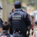 Dois guardas municipais escoltando crianças em área urbana movimentada durante o dia.
