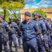 Grupo de Guardas Municipais alinhados em fila vestindo uniforme azul com colete tático em área externa.