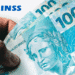 Cédulas de 100 reais com logo do INSS no canto superior esquerdo.