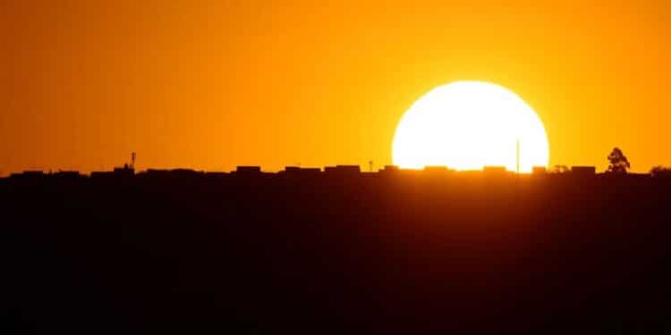 Sol intenso em tons de laranja e amarelo, formando a silhueta de uma cidade, representando a discussão sobre o possível retorno do Horário de Verão em novembro de 2025 e o aproveitamento da luz do dia.