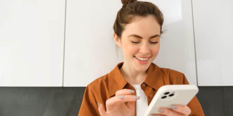 Mulher jovem e sorridente interagindo com um smartphone branco, ponderando decisões sobre a escolha do celular.