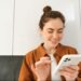Mulher jovem e sorridente interagindo com um smartphone branco, ponderando decisões sobre a escolha do celular.