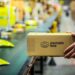 Mão segurando uma caixa do Mercado Livre em uma esteira de centro de distribuição, simbolizando as 20 mil novas vagas de emprego da empresa, especialmente em Logística.