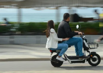 Homem e mulher pilotando juntos uma moto elétrica preta e branca em uma avenida urbana