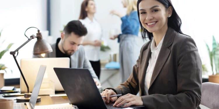 Jovem administradora sorrindo no escritório com laptop, representando as oportunidades de carreira em 2025